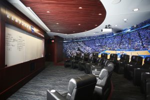Joe Craft Center - Marksbury Player's First Men's Basketball Locker Room tiered team meeting room with custom millwork and wall graphics, and projection screen with surround sound.